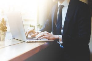 Man wearing suit uses laptop at wooden table